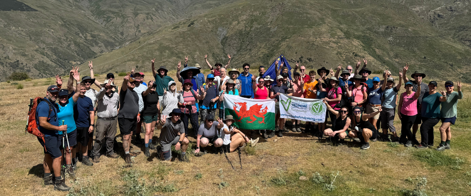 A large group of people are stood together on a mountian during a trek.
