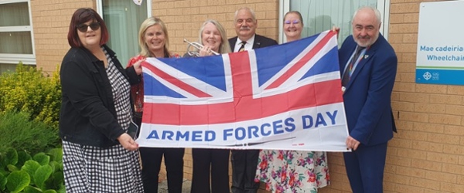 A group of people are holding an Armed Forces Day flag.