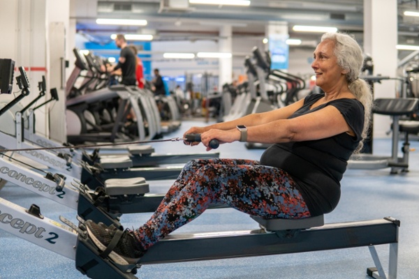 A woman is in the gym and exercising on a rowing machine.
