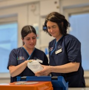 two research nurses wearing blue uniforms standing behind a bench looking at a saline bag