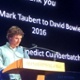 A man is reading from a lectern on a stage, The screen behind him says: "Thank you, Mark Taubert to David Bowie 2016, Benedict Cumberbatch