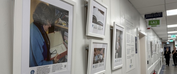 Images from the art exhibition are hung in white frames on a wall in a hospital corridor.
