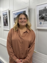 A woman is smiling and standing next to an art exhibition.
