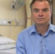 A man in a blue shirt is sat in a hospital room.